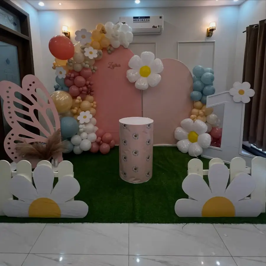 Birthday stage with giant daisies, a butterfly cut-out and pastel balloons on artificial grass