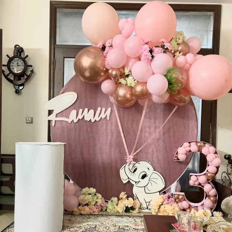 Round pink birthday backdrop with an elephant, a name sign and a cluster of pink balloons