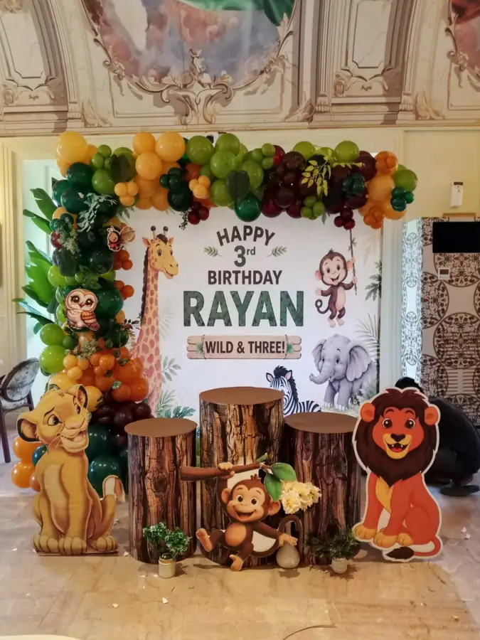 Jungle birthday setup with lion and monkey cut-outs, tree stumps and a flower and leaf arch