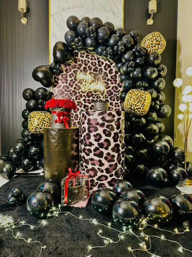 Black balloon arch around a leopard-print panel with fairy lights