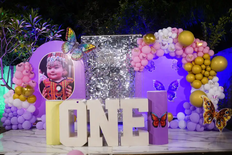 First birthday stage with large ONE letters, a sequin wall and purple, pink and gold balloons