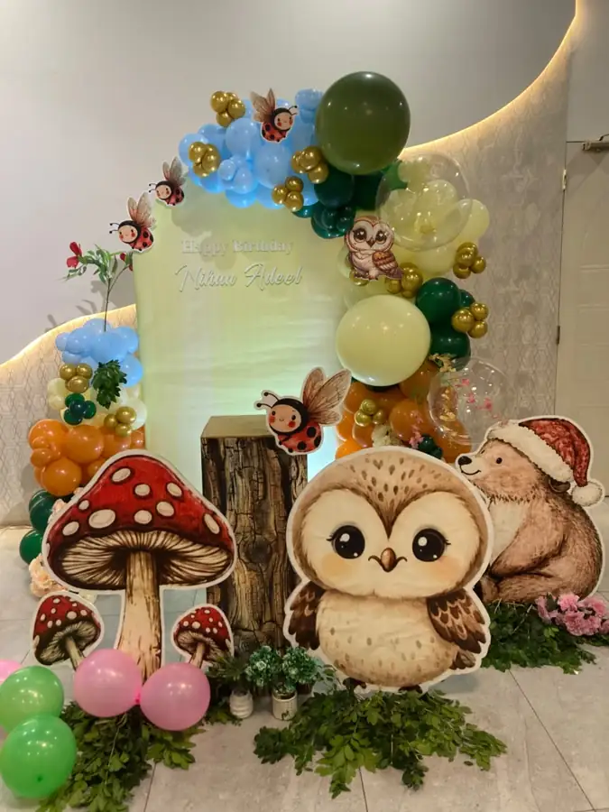 Woodland birthday setup with large owl and mushroom cut-outs and a green balloon arch