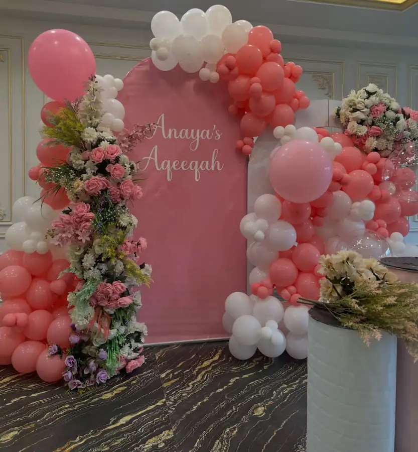 Pink and white balloon arch with fresh flowers around a pink backdrop