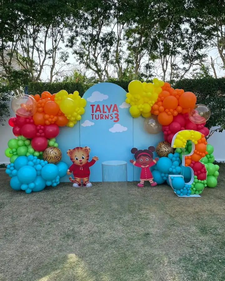 Outdoor birthday backdrop with a rainbow-coloured balloon garland on a lawn