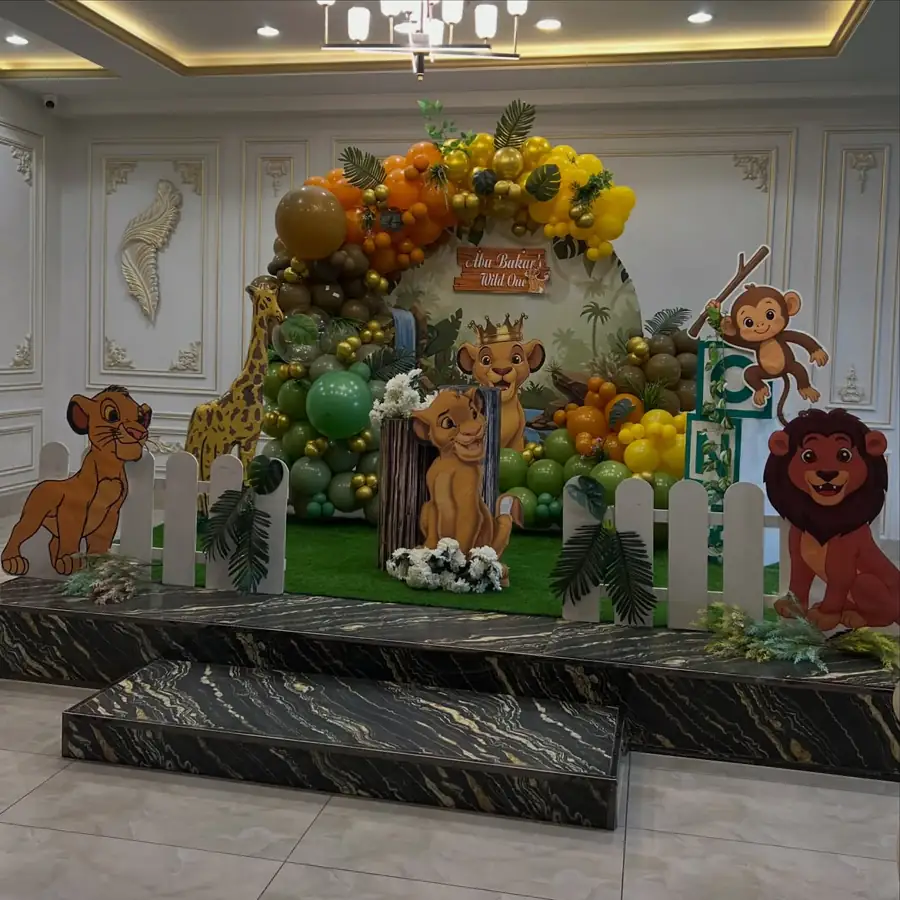 Safari jungle birthday stage with Lion King characters and an orange and green balloon arch