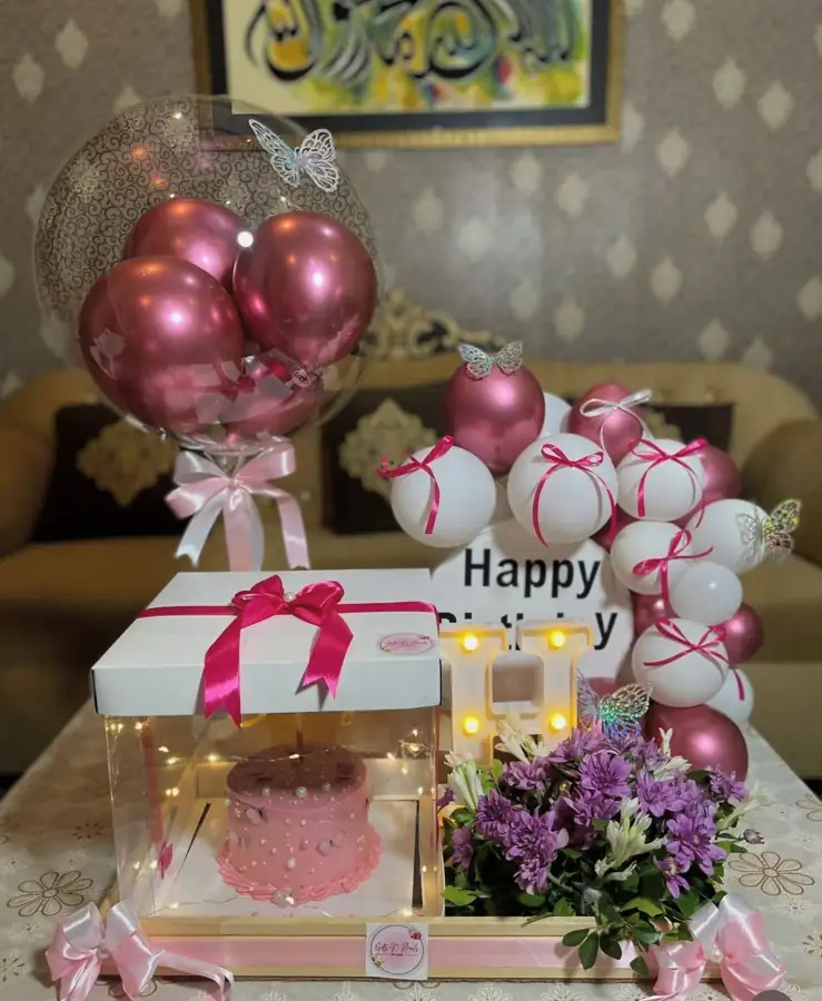 Gift box with a pink chrome balloon, flowers and a cake on a table