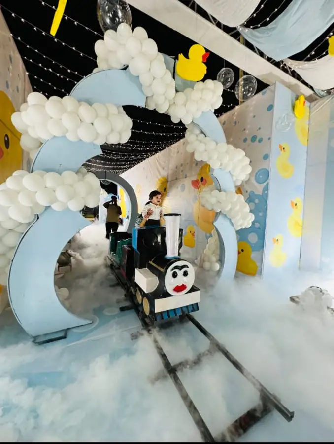 Child riding a mini train on a track surrounded by a white balloon decor