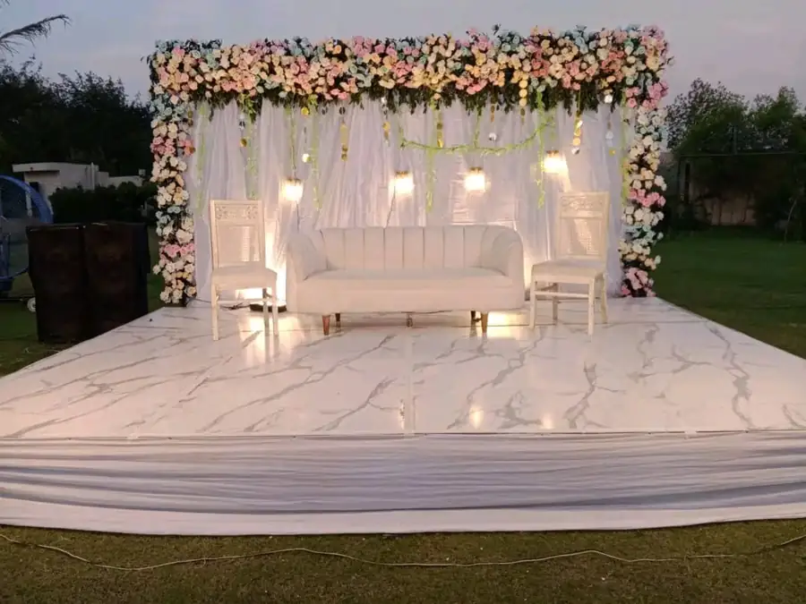 Outdoor engagement stage with a white floral arch and white sofa at dusk