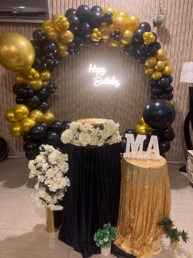 Black and gold balloon ring with a neon Happy Birthday sign, flowers and letter lights