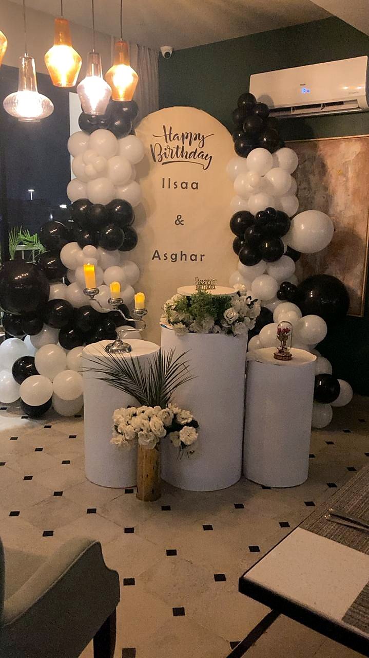 Black and white balloon birthday setup with cylinder stands and a name backdrop