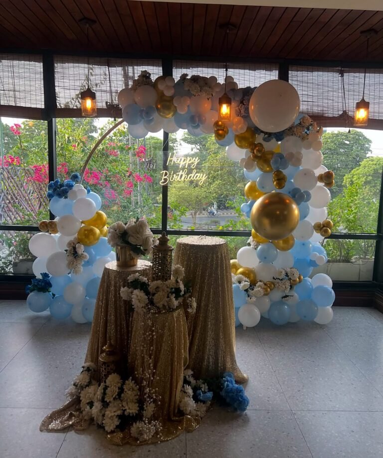 Light blue and gold balloon arch with a draped cake table in a garden lounge