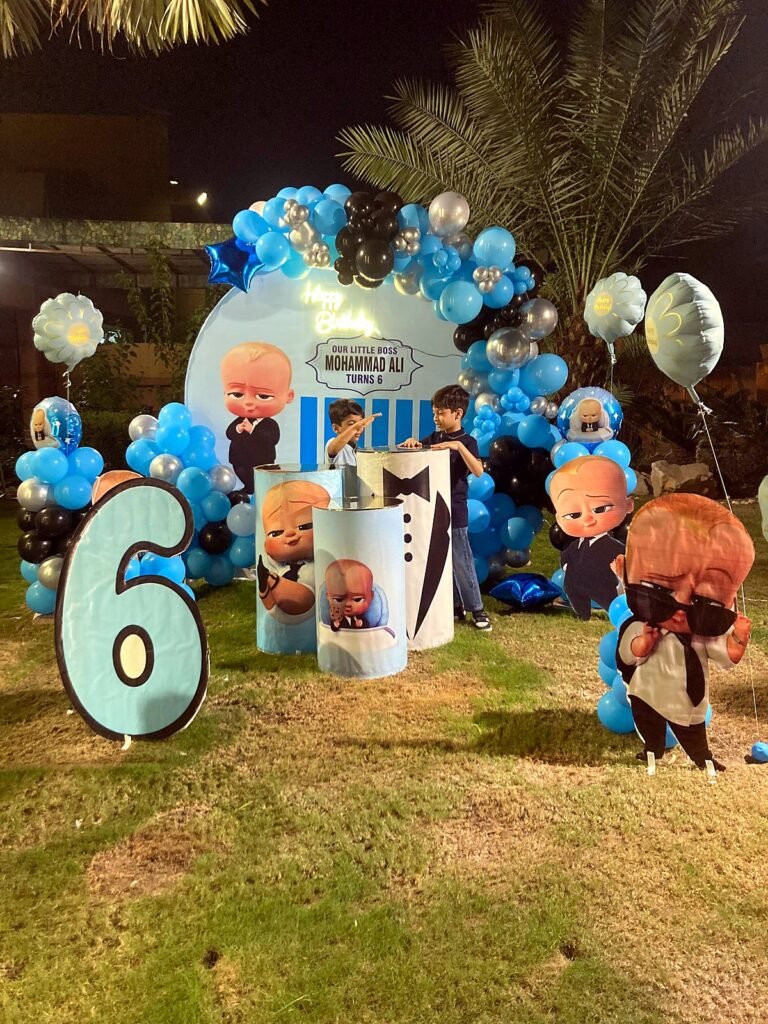 Boss Baby themed birthday setup on a lawn at night with blue balloons, a number six and character cut-outs