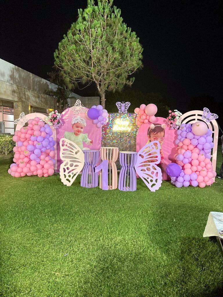Pink and purple butterfly birthday setup on a lawn with balloon panels and lights