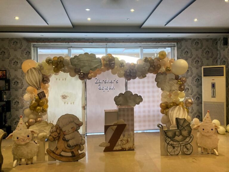 Cream and gold first birthday setup with a balloon arch, teddy and rocking props