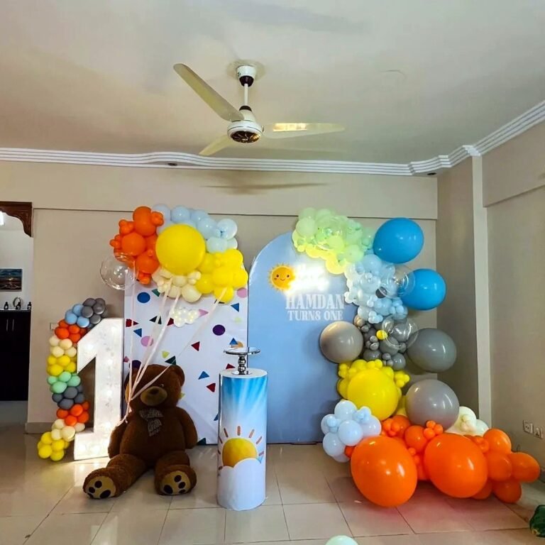 Colourful first birthday setup with a number one balloon, teddy bear and sun backdrop
