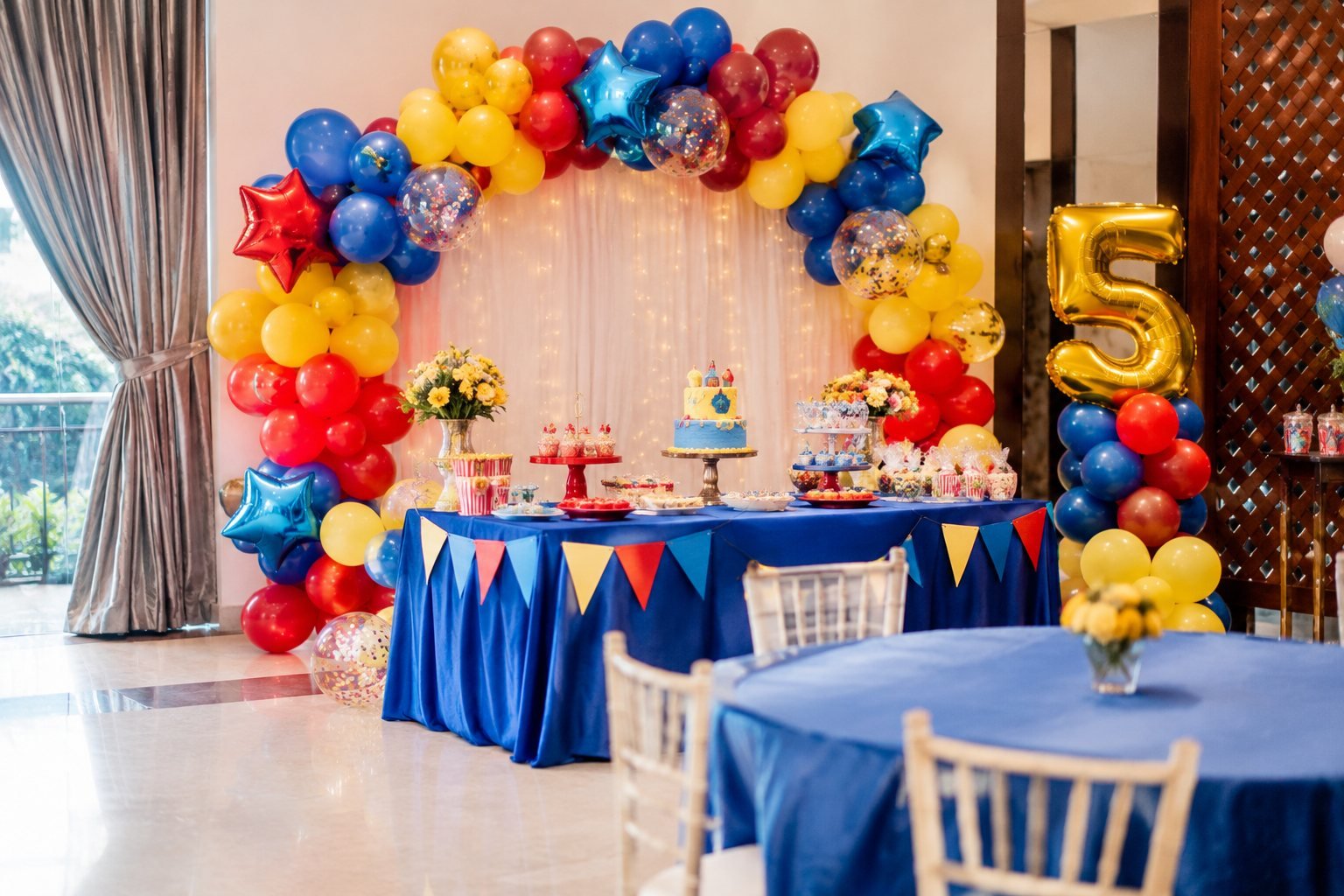 Kids birthday party hall with a red, yellow and blue balloon arch and dessert table