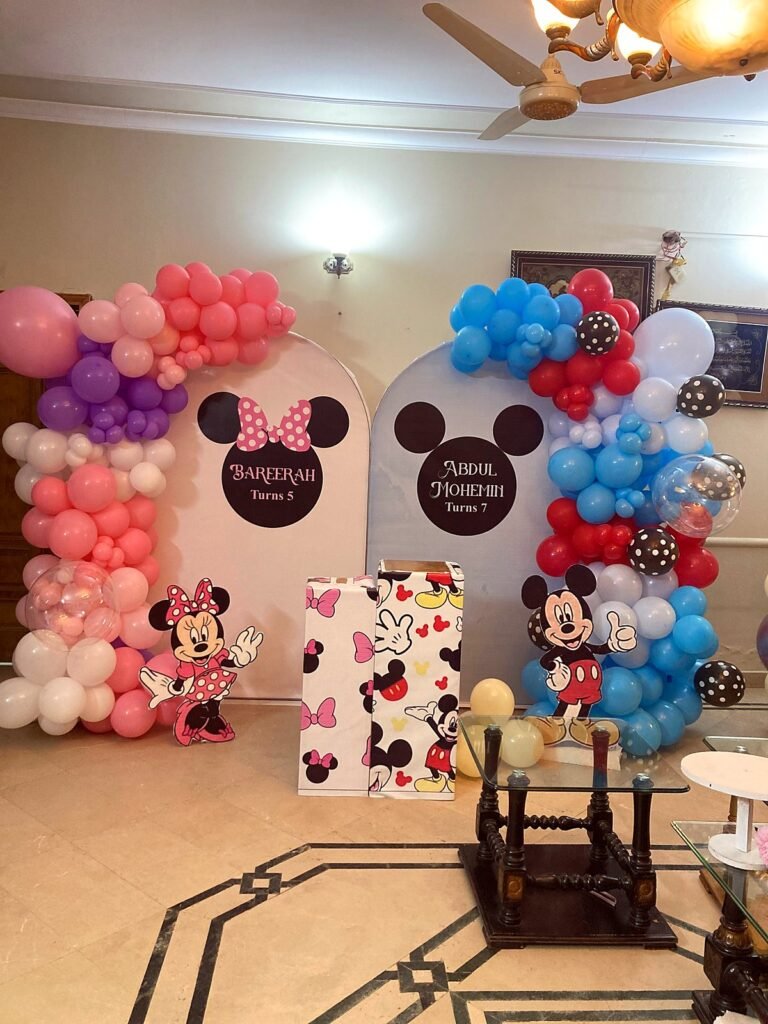 Mickey and Minnie birthday setup with pink, blue and black balloon arches and name panels