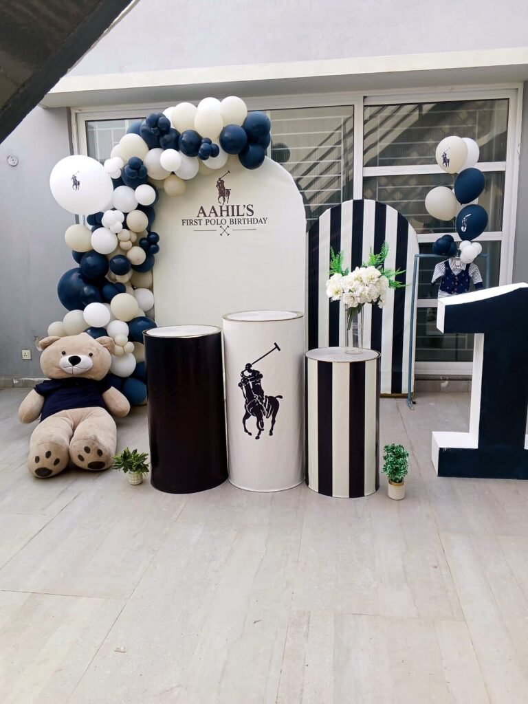 Navy and white balloon arch with striped backdrop, teddy bear and a number one