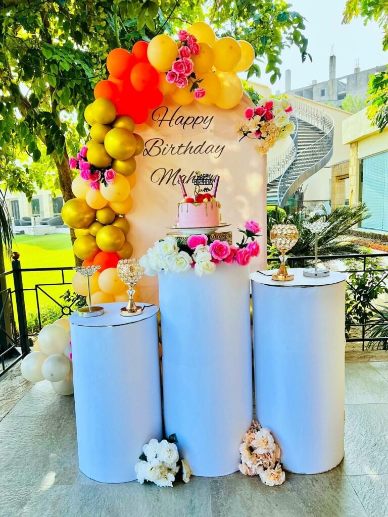 Orange, gold and pink balloon arch with blue cake stands and flowers outdoors