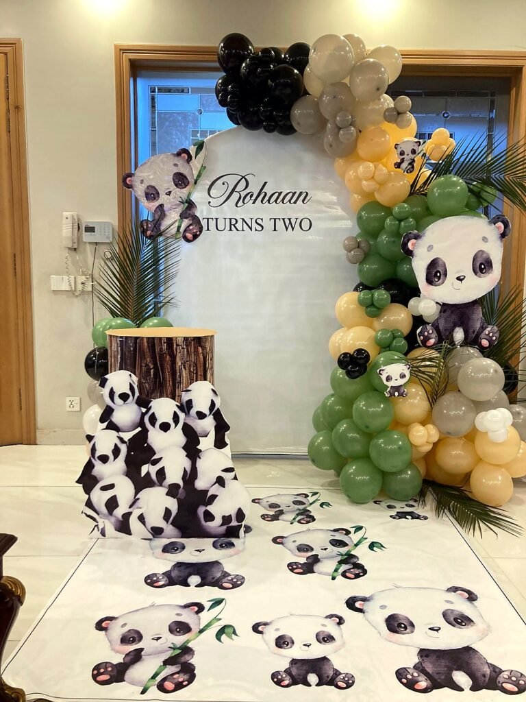 Panda themed second birthday setup with green and black balloons, panda cut-outs and a name panel