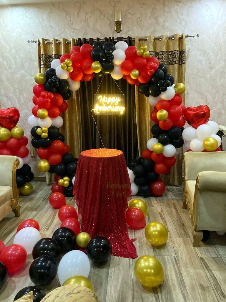 Red, black and gold balloon ring with a neon Happy Birthday sign and a draped cake table