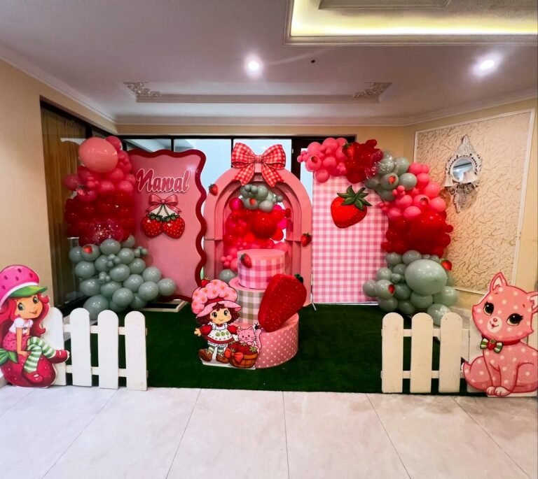 Strawberry theme birthday backdrop with red and pink balloons and a white picket fence