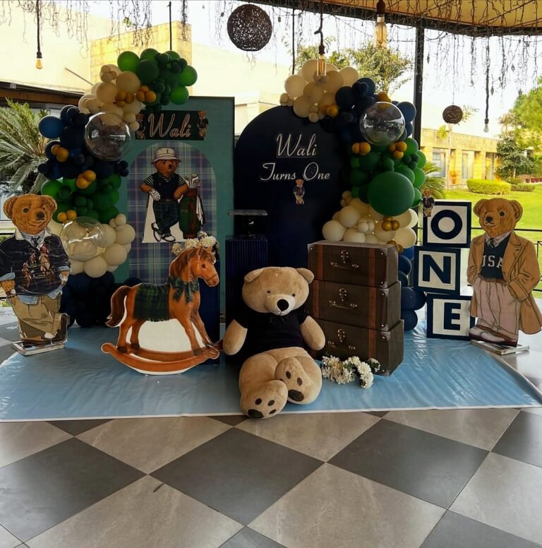 Teddy bear and vintage suitcase theme first birthday setup with a green balloon arch