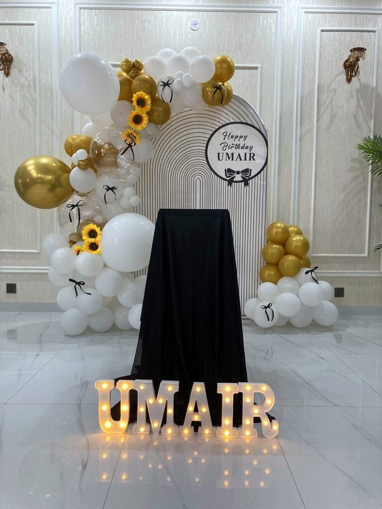 White and gold balloon arch with lit marquee letters and sunflowers